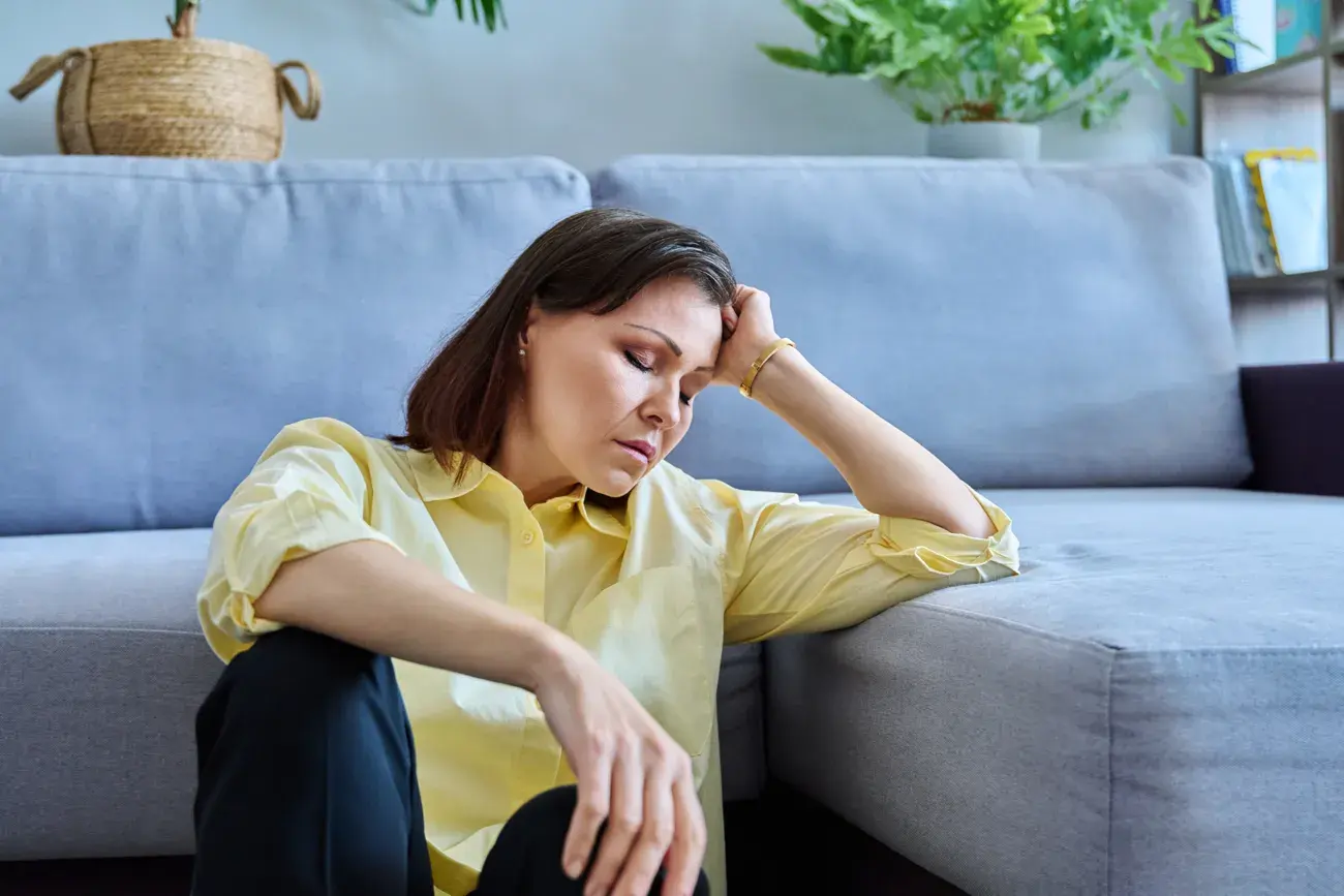 Tired woman resting her head on her hand while sitting by a sofa